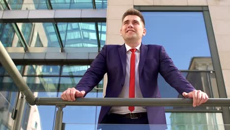 Businessman-is-leaning-on-railing-near-building.