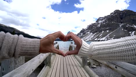 Young-couple-on-log-bridge-making-heart-shape-frame