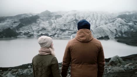 Back-view-of-young-couple-standing-in-Ice-lagoon.-Traveling-man-and-woman-exploring-the-Iceland-together