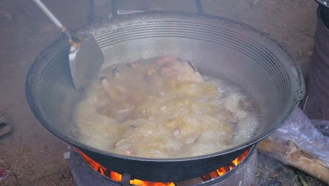 Stir-frying-chickens-in-a-large-wok-cooking-on-a-charcoal-and-wood-brazier-stove-outdoors