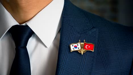 Geschäftsmann-zu-Fuß-in-Richtung-Kamera-mit-Freund-Land-Flaggen-Pin-Südkorea---Türkei