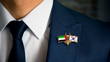 Businessman-Walking-Towards-Camera-With-Friend-Country-Flags-Pin-United-Arab-Emirates---South-Korea