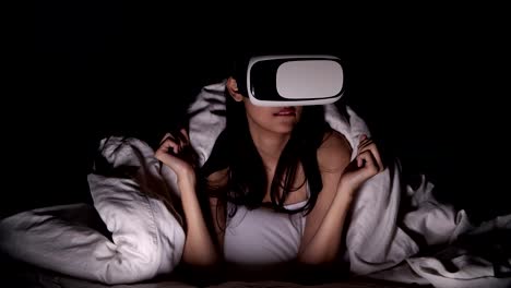 Woman-watching-VR-horror-movie-alone-in-bed.-Asian-woman-lying-in-bed-alone-wearing-VR-head-set,-very-surprise-and-shock-from-scary-movie.-High-tech-Halloween-home-alone-concept.