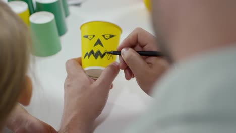 Man-Drawing-Spooky-Face-on-Halloween-Cup