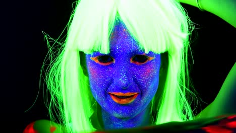 Woman-with-UV-face-paint,-wig,-glowing-clothing-dancing-in-front-of-camera,-face-close-up-of-make-up.-Caucasian-woman.-.