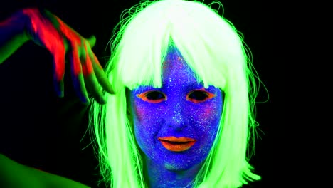 Woman-with-UV-face-paint,-wig,-glowing-clothing-dancing-in-front-of-camera,-face-close-up-of-make-up.-Caucasian-woman.-.