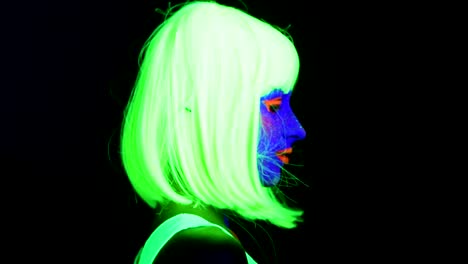 Woman-with-UV-face-paint,-wig,-glowing-clothing-portrait-turnaround-toward-camera,-face-close-up-of-make-up.-Caucasian-woman.-.