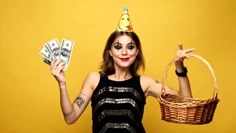 Carefree-lady-with-halloween-make-up-holding-in-hands-candies-and-money-and-choose-money-isolated-over-yello