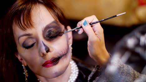 Halloween-partido,-primer-plano,-Maquillaje-artista-dibuja-un-maquillaje-terrible-en-la-cara-de-una-mujer-morena-para-una-fiesta-de-Halloween.-se-ve-el-paisaje-en-el-estilo-de-Halloween