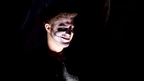 Halloween-party,-night,-frightening-portrait-of-a-man-in-the-twilight,-in-the-rays-of-light.-man-with-a-terrible-make-up-in-a-black-witch-costume