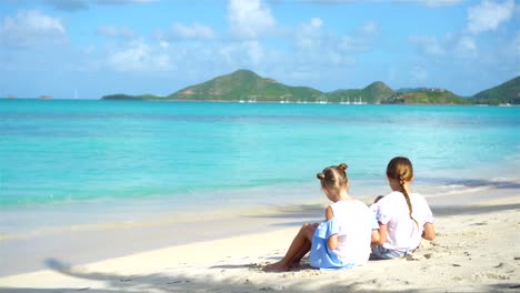 Zwei-kleine-glückliche-Mädchen-haben-eine-Menge-Spaß-am-tropischen-Strand-mit-Sand-spielen