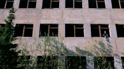 Woman-sitting-on-window-of-destroyed-multi-storey-building-with-many-broken-windows.