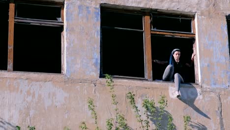 Woman-sitting-on-window-of-destroyed-multi-storey-building-with-many-broken-windows.