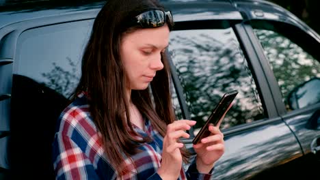 Mujer-envía-un-mensaje-en-el-teléfono-de-pie-al-lado-del-coche.