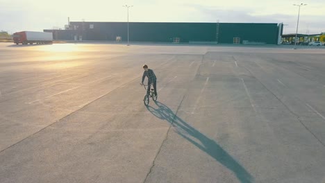 cámara-de-jinete-joven-adolescente-masculino-del-vuelo-en-la-bicicleta-de-bmx-en-el-lugar-vacío-urbano-que-nadie-de-asfalto