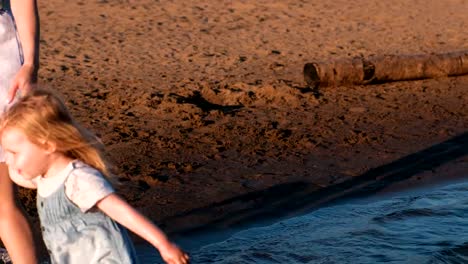 Mutter-und-Mädchen-spielen-am-Strand-des-Flusses-bei-Sonnenuntergang-und-Schwimmen.