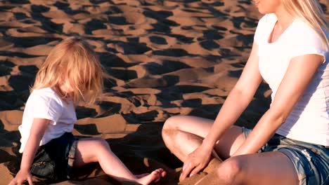 Hija-y-mamá-rubia-hermosa-juegan-con-arena-sentados-juntos-en-la-playa.