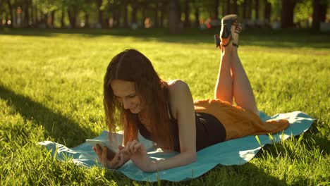 Attractive-lady-laying-down-over-green-grass-while-typing-a-message-on-phone