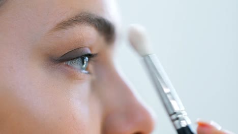 Extreme-close-up-visagiste-applying-eye-shadows-using-cosmetic-brush-to-face-teenage-model