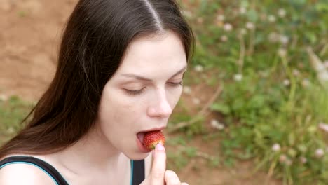 Young-woman-brunette-eats-a-strawberry-sitting-on-the-beach.-Side-view.