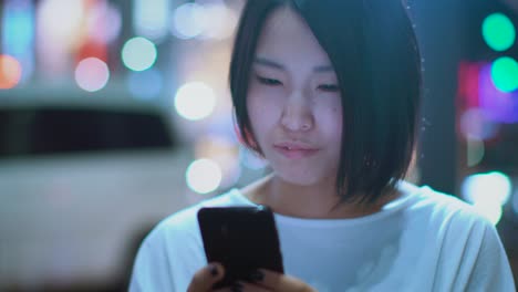 Retrato-de-la-chica-japonesa-atractiva-Ropa-Casual-usa-Smartphone.-En-el-fondo-gran-ciudad-publicidad-vallas-publicitarias-luces-brillan-en-la-noche.