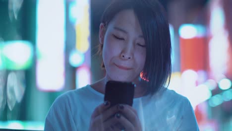 Porträt-von-die-attraktive-Japanerin-mit-Piercing-und-lässige-Kleidung-nutzt-Smartphone.-Im-Hintergrund-Plakate-Großstadt-Werbung-Lichter-leuchten-in-der-Nacht.