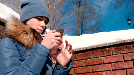 Frau-ist-eine-Nachricht-auf-dem-Handy-sitzt-im-Winterpark-eingibt.