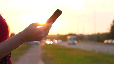 Weibliche-Hand-mit-Smartphone-gegen-das-fahren-Autos-auf-die-Straße