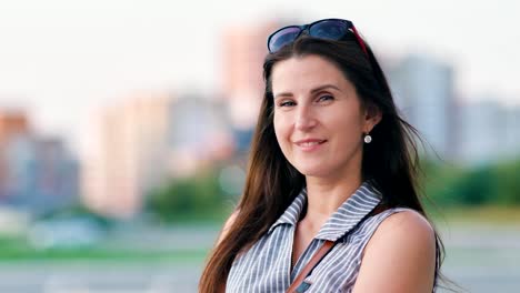 European-woman-with-sunglasses-on-head-smiling-standing-at-downtown-of-summer-modern-city