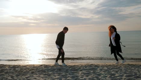 Young-trendy-man-and-woman,-people-on-sand-beach,-happy-married-adult-couple-having-fun,-playing,-fooling-by-the-sea-in-spring-or-autumn.-Warm-sunny-day