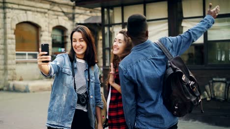 Aufgeregt,-dass-junge-Menschen-online-video-Anruf-mit-Smartphone-Gadget-zu-halten-und-im-Gespräch-zeigt-Gebäude-dahinter-machen-Daumen-hoch-positive-Gefühle-zeigen.