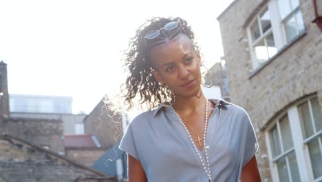 Fashionable-young-black-woman-in-blue-dress-standing-in-sunlight-on-the-street,-backlit,-low-angle