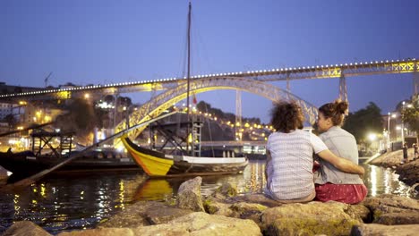 Couple-sitting-on-stones,-hugging-and-kissing-on-embankment