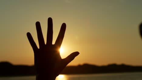 Silhouette-Of-Woman-Making-Flare-Shape-With-Hands-Against-Sun