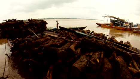 Barcos-con-pilas-de-leña-niño-indio-se-encuentra-en-pequeños-Cogs-de-corteza-en-el-muelle-del-río-Ganges-alta-agua-Manikarnika-quema-Ghat