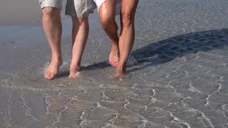 Cámara-lenta-Recortar-imagen-de-patas-de-Pareja-caminando-por-el-agua-en-la-playa,-Sudáfrica