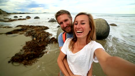 Young-couple-stand-near-Moeraki-boulders-and-take-selfie-portrait