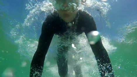 SLOW-MOTION-CLOSE-UP:-Happy-young-surfer-duck-diving-under-the-wave