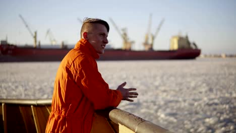 Young-man-in-orange-uniform-traveling-on-board-of-the-ship-in-winter.