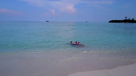 v04037-Aerial-flying-drone-view-of-Maldives-white-sandy-beach-2-people-young-couple-man-woman-romantic-love-on-sunny-tropical-paradise-island-with-aqua-blue-sky-sea-water-ocean-4k