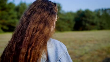 mujer-de-pelo-castaño-la-manera-es-caminando-sobre-una-naturaleza-cerca-del-bosque-en-día-de-verano,-vista-media-vuelta