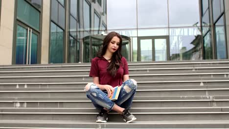 Young-girl-reading-a-book-sitting-on-steps-at-city