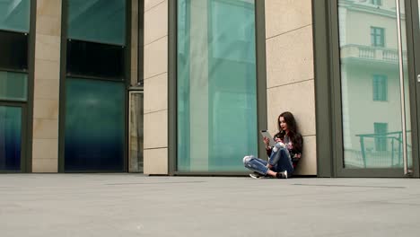 Chica-sentada-en-suelo-con-tableta,-apoyado-en-la-pared