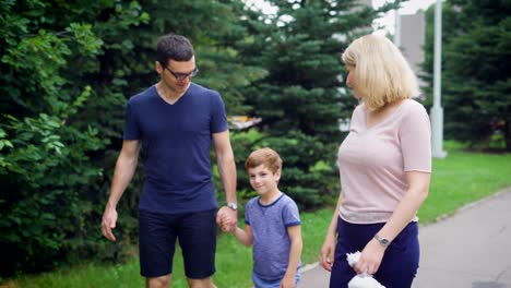 Nahaufnahme-der-glückliche-Familie-zusammen-auf-der-Straße-lachen-gehen.-Vater-und-Mutter-einander-und-Sohn-sprechen.-Liebende-Paar-und-ihr-Kind-auf-dem-Weg-mit-Bäumen-im-Hintergrund-treten