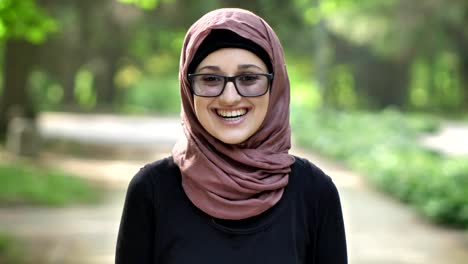 Portrait-of-a-young-laughing-girl-in-glasses-wearing-hijab,-outdoor,-in-a-park-in-the-background.-50-fps