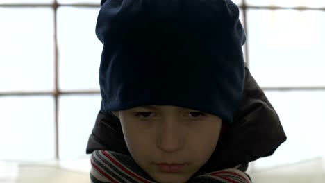 portrait-emaciated-refugee-boy-stands-alone-near-a-broken-window,-looking-into-the-camera