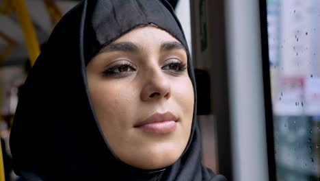 Gesicht-des-jungen-süßen-Muslima-Hijab-ist-gerade-im-verregneten-Fenster-im-Bus,-Transportkonzept,-städtebauliche-Konzept,-Wetter-Konzept,-Konzept-träumen