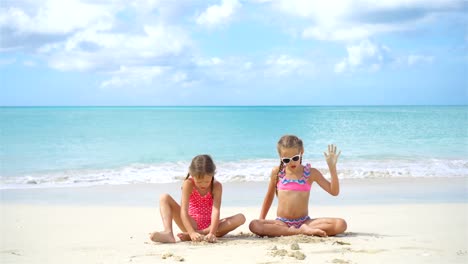 Zwei-kleine-glückliche-Mädchen-haben-eine-Menge-Spaß-am-tropischen-Strand-mit-Sand-spielen