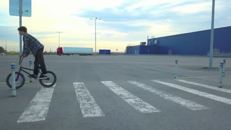 flying-4k-shot-of-young-teenager-in-casual-doing-a-jump-trick-on-a-bmx-bike-going-on-a-street-crosswalk-in-the-city