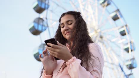 Das-Mädchen-nutzt-ein-Smartphone-steht-nahe-dem-Riesenrad.-4K.-Close-up